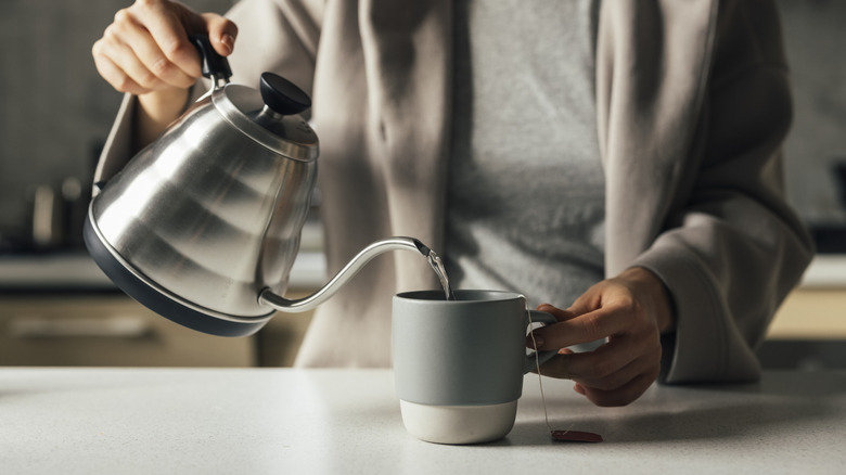 Hands pour water from kettle into cup