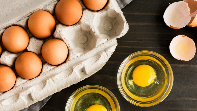 a carton of eggs next to a small glass with a cracked egg