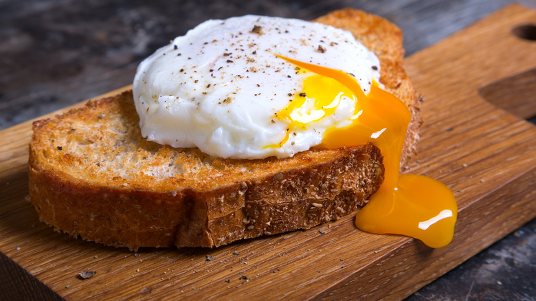 Runny poached egg on toast on a wooden board