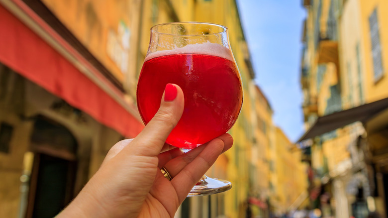 Holding a glass of bright red lambic beer on a city street