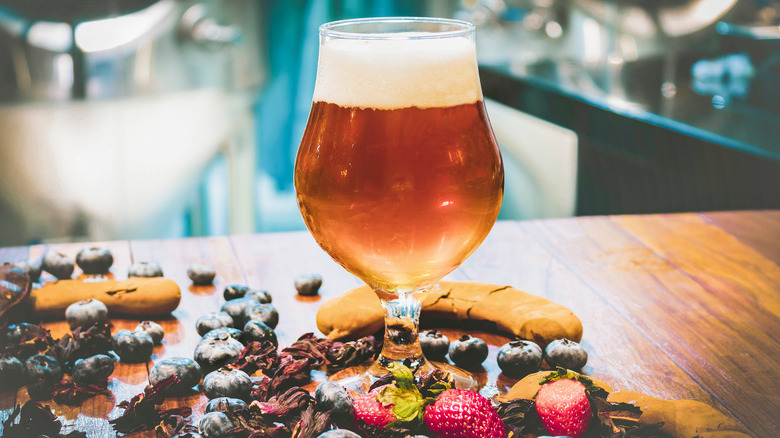 Glass of fruity beer surrounded by fruit on a counter