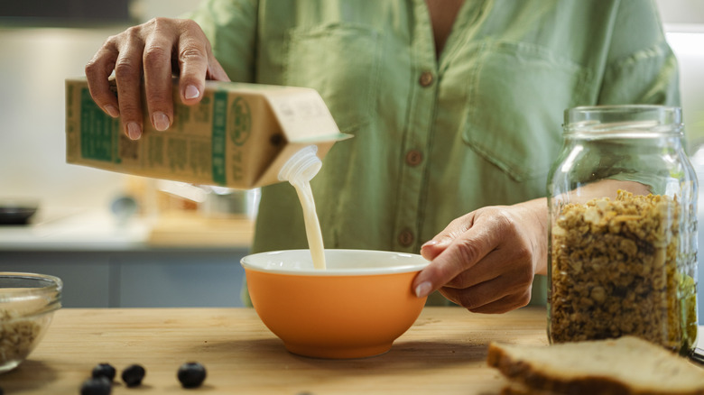 Woman pouring carton of milk into orange bowl