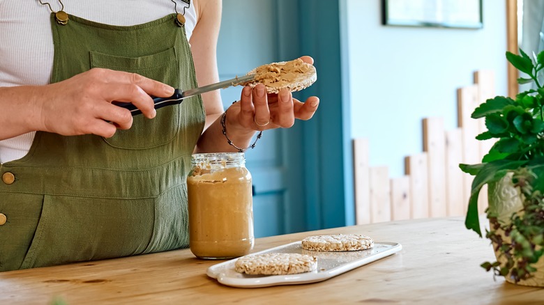 woman spreading peanut butter on rice cake