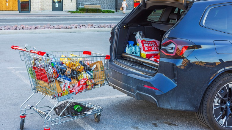 A shopping cart with groceries next to the open trunk of a car