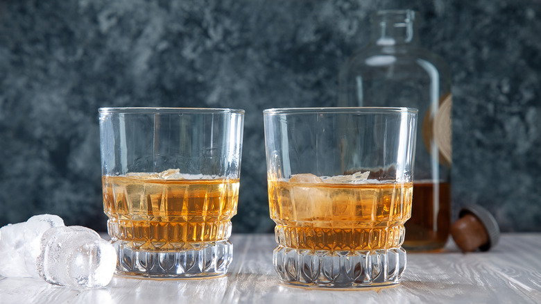 two glasses of bourbon in front of an open bourbon bottle