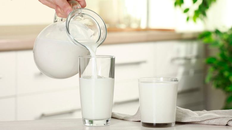 Hand pouring milk into a cup from a pitcher