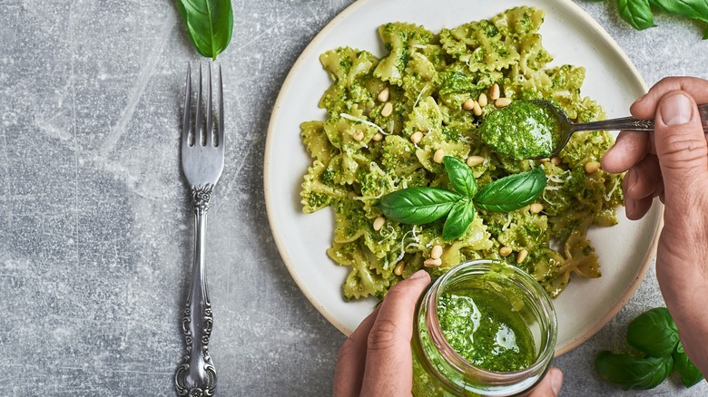 Person spooning pesto onto a plate of pasta
