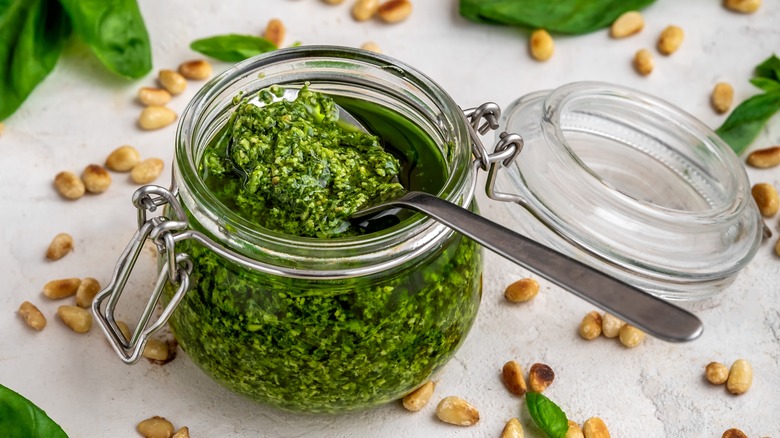 Open pesto jar with a spoon surrounded by ingredients