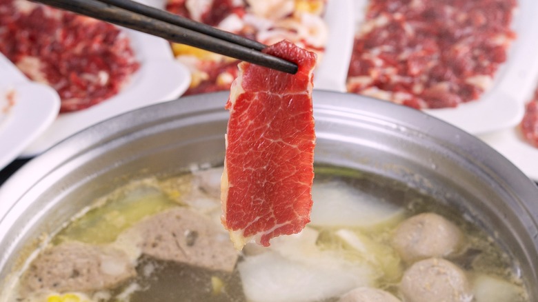 Chopsticks dipping raw beef into hot pot broth