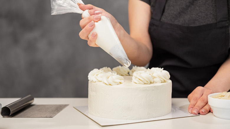 Person frosting a white cake