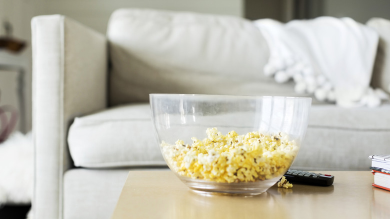 A bowl of popcorn on a coffee table in front of a cozy sofa.