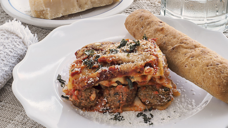 Lasagna with whole meatballs on white plate with bread