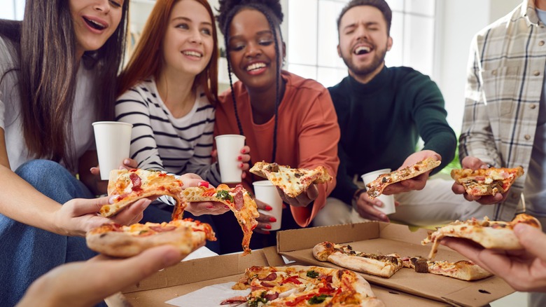 Happy people serve themselves pizza from a pizza box