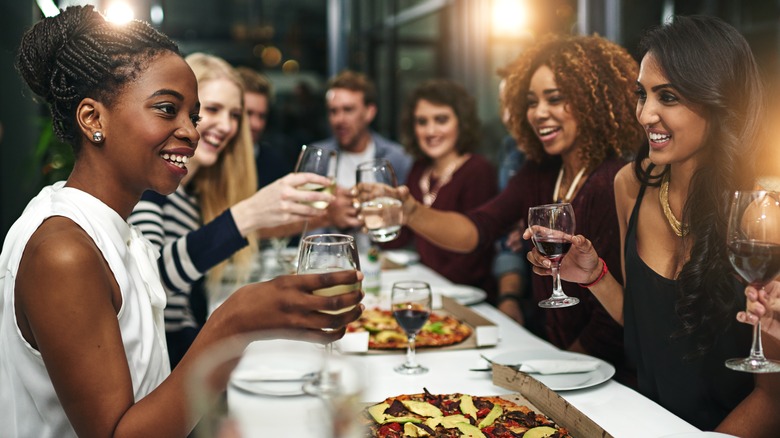 Smiling friends toast with wine glasses at a pizza party