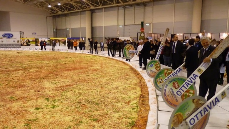 People surrounding a large pizza