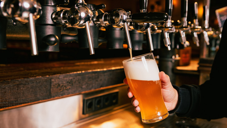 A bartender pours a beer from a tap with too much foam.