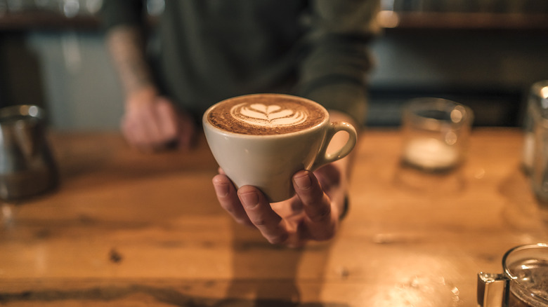 A barista holding a cup of coffee at a coffee shop.