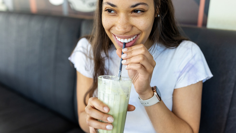 A young woman drinks an iced matcha latte through a straw