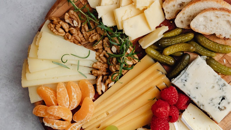 Board with cheese, fresh fruit, pickles, and herbs