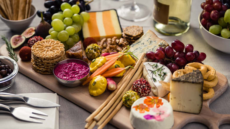 Serving board with various cheeses, fruits, dips, and crackers