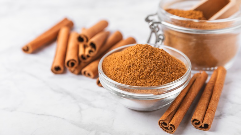 Ground cinnamon in bowl and cinnamon sticks