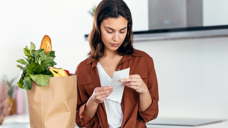 woman looks at grocery receipt next to bag of groceries