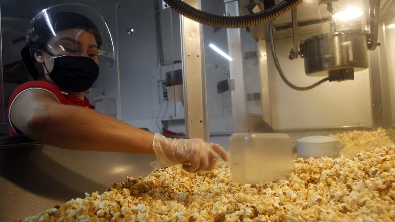 A worker scooping popcorn out of a machine in a cinema snack bar.