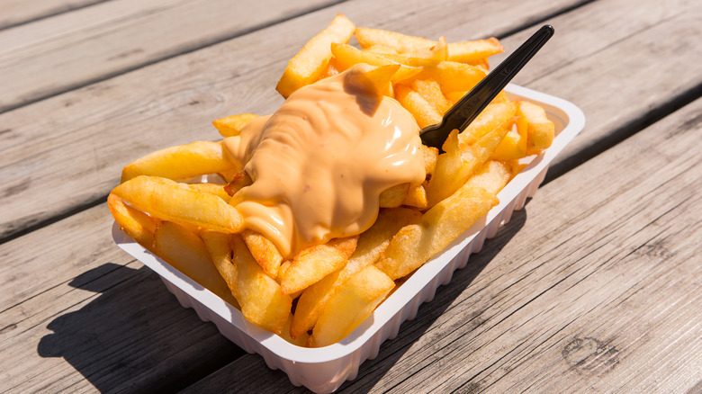 Fries topped with andalouse sauce on a table.