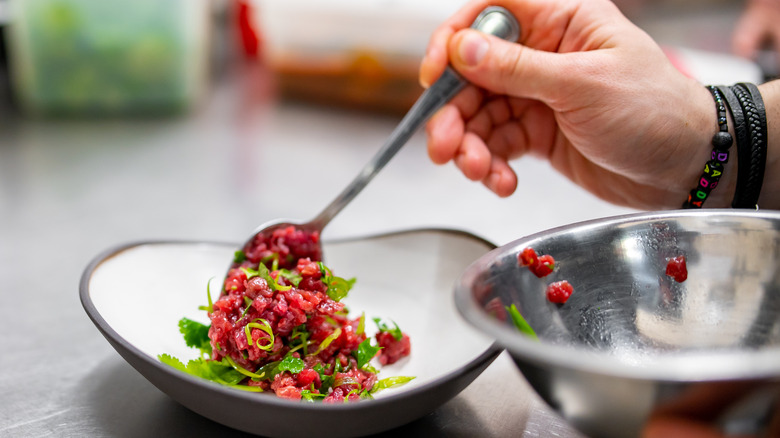 A hand mixes tartare in a bowl with a spoon.