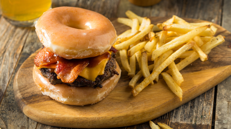 Doughnut bacon cheeseburger with fries on wooden board