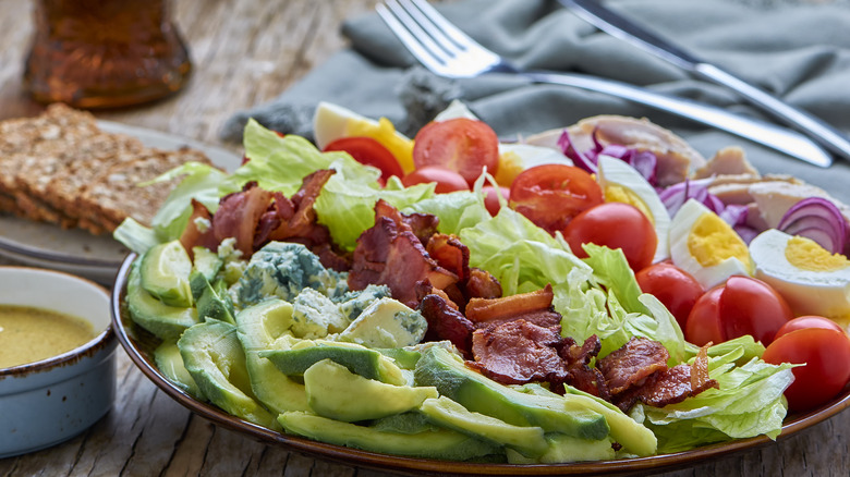 Plate of Cobb salad with silverware and other dishes in background