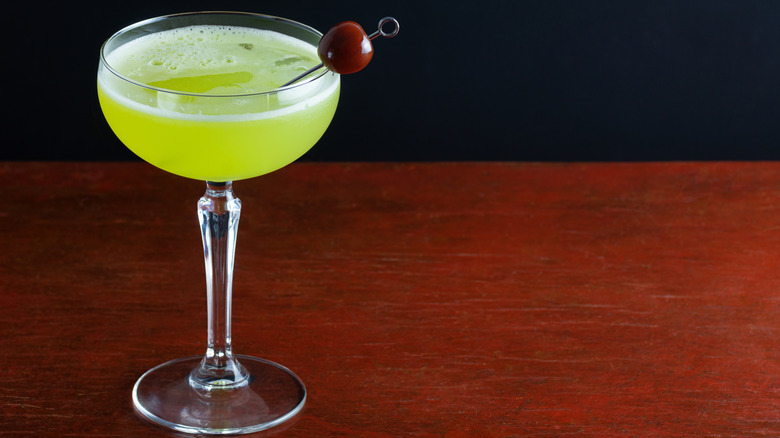 The Last Word cocktail with cherry garnish in a stemmed glass against a wood background