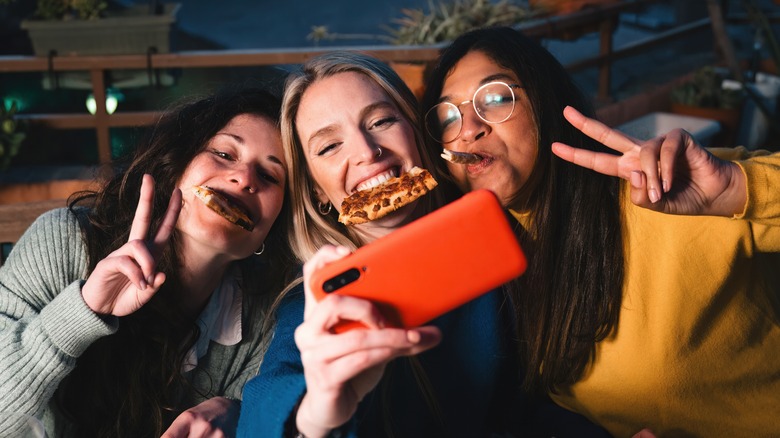 Friends taking selfie while eating pizza