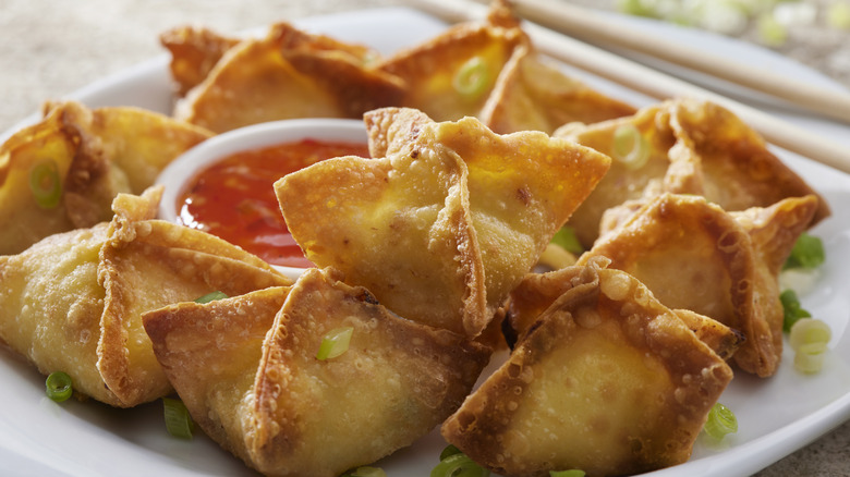 A plate of fried wontons surrounding a cup of dipping sauce