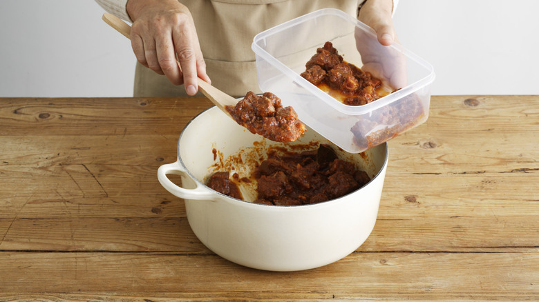 A person putting leftover stew into a plastic container.