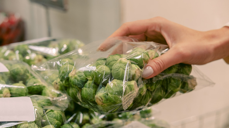 Hand grabbing plastic package of Brussels sprouts at store