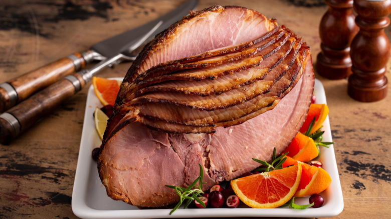 Spiral-sliced ham on a platter with fruits and herbs