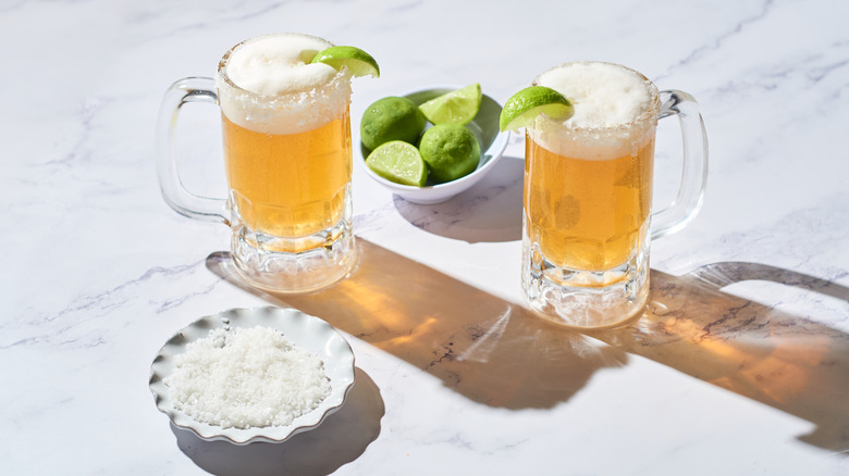 Two cheladas next to a bowl of limes and a bowl of salt