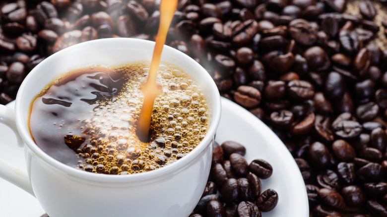 Pouring cup of coffee amidst coffee beans