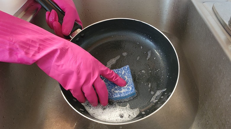 gloved hands washing black pan