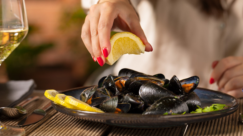 woman squeezing lemon on mussels