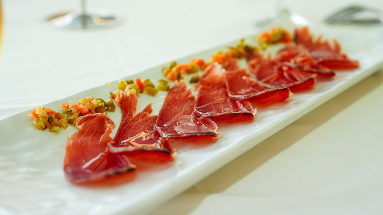 Slices of mojama, dry cured tuna, artfully presented on a white plate.