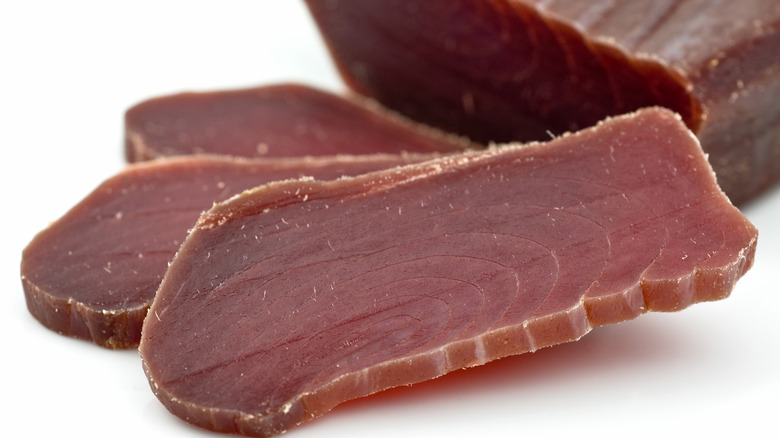 Thin slices of cured tuna, a deep vermillion color, showing the grain of the meat.