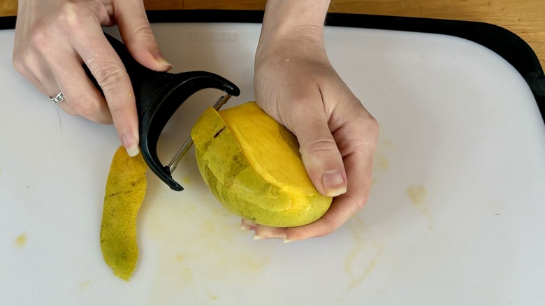 Hands peeling whole mango