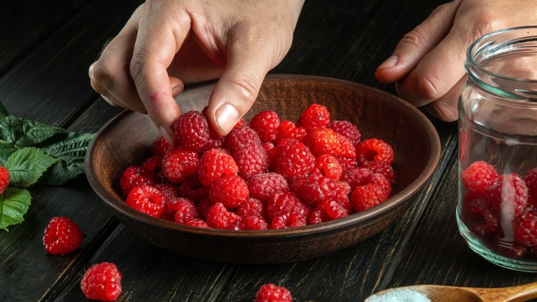 Hand holding raspberry from a bowl