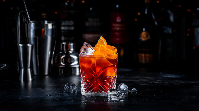 a negroni in a sophisticated glass, topped with a twisted orange rind, on a glossy black table