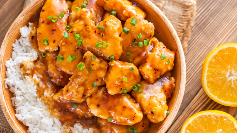 Bowl of orange chicken and rice with sliced orange