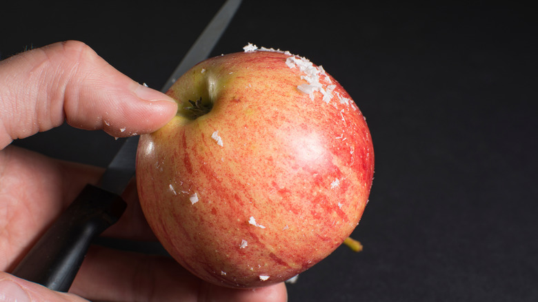 Hand using paring knife to remove wax from an apple