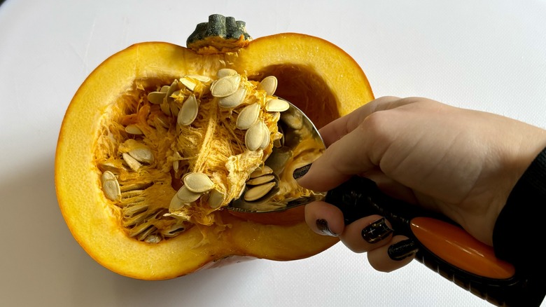 Hand scooping seeds from halved pumpkin