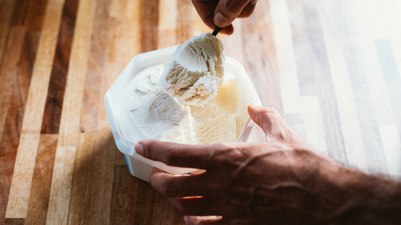 hands scooping vanilla ice cream out of a tub